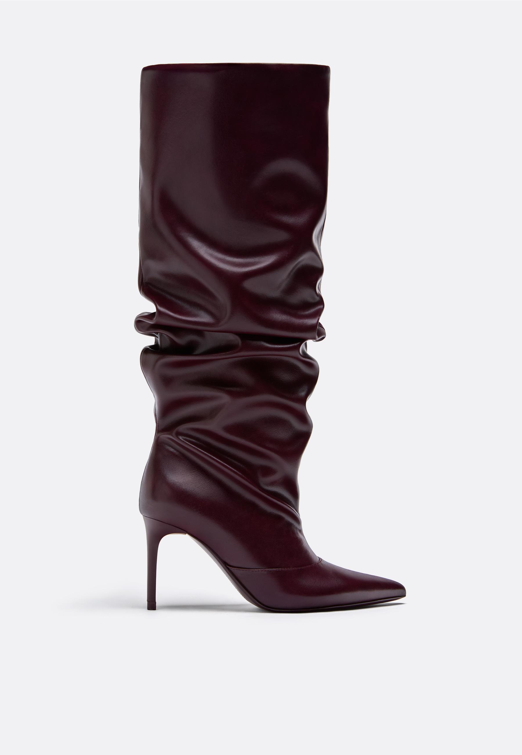 Side view of a burgundy high boot with a stiletto heel and pointed toe, ruched design on the shaft.